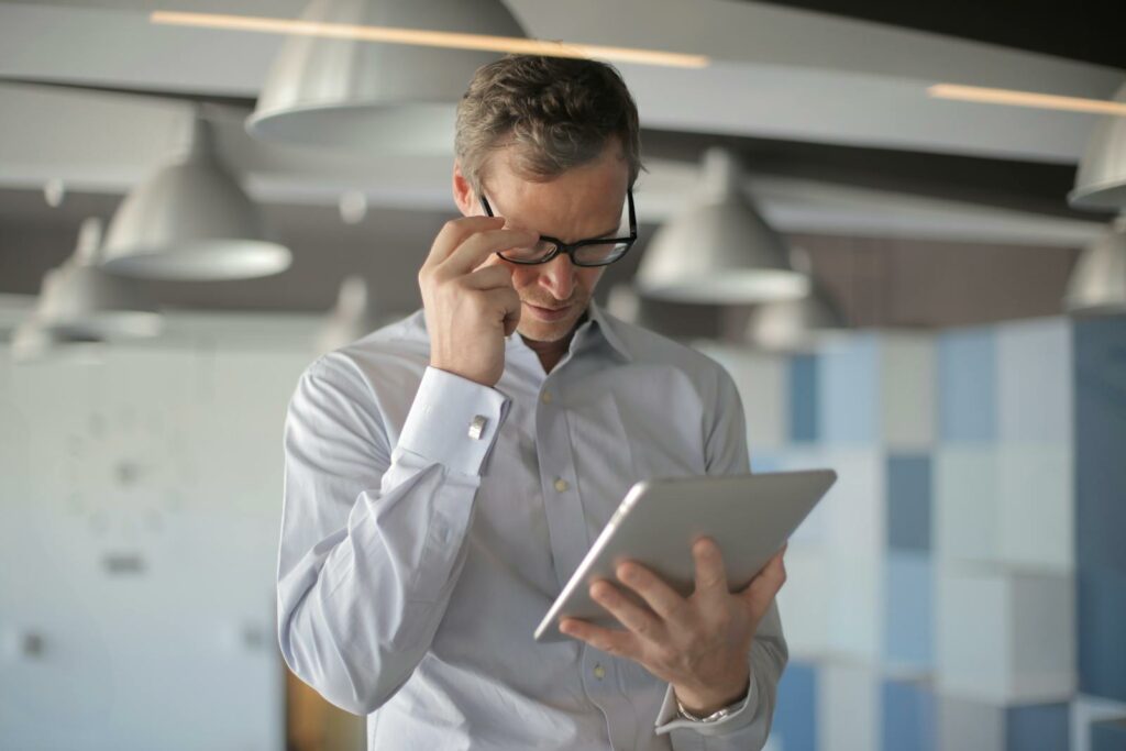 Professional man in eyeglasses focusing on tablet device in a stylish office setting.